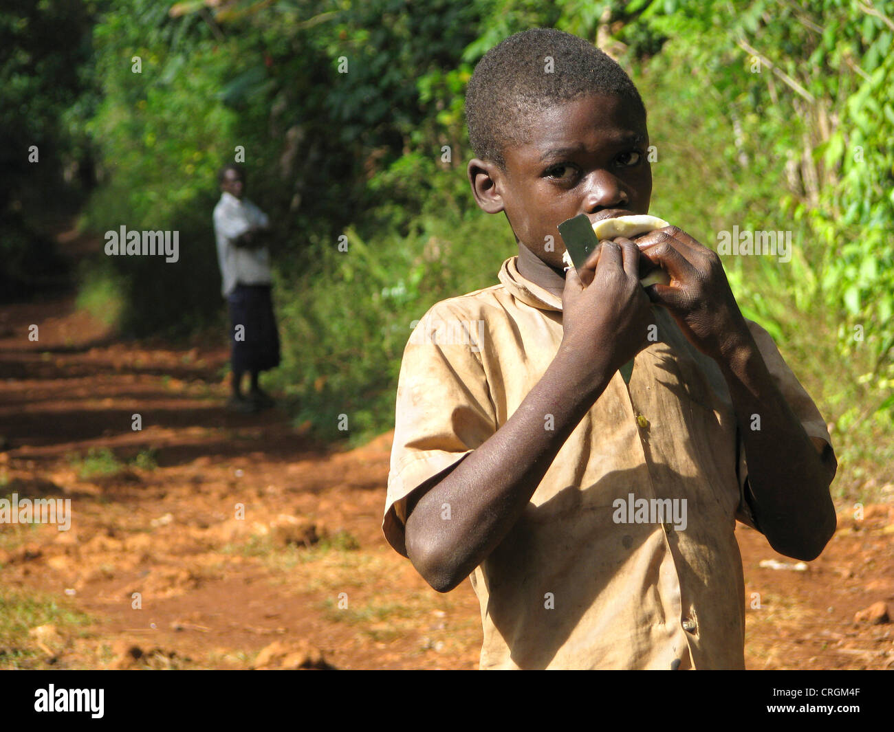 Junge im ländlichen Raum ist das Saugen an eine Orange, Uhren Mann im Hintergrund, Haiti, Grande Anse, Jeremie Stockfoto