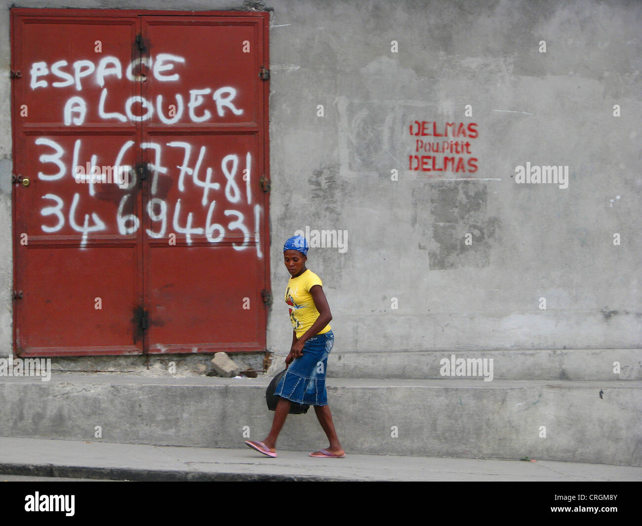 Frau zu Fuß entlang einer Betonwand mit einer eisernen Tür bietet Platz für Miete, Haiti, Provinz de l ' Ouest, Delmas, Port-Au-Prince Stockfoto