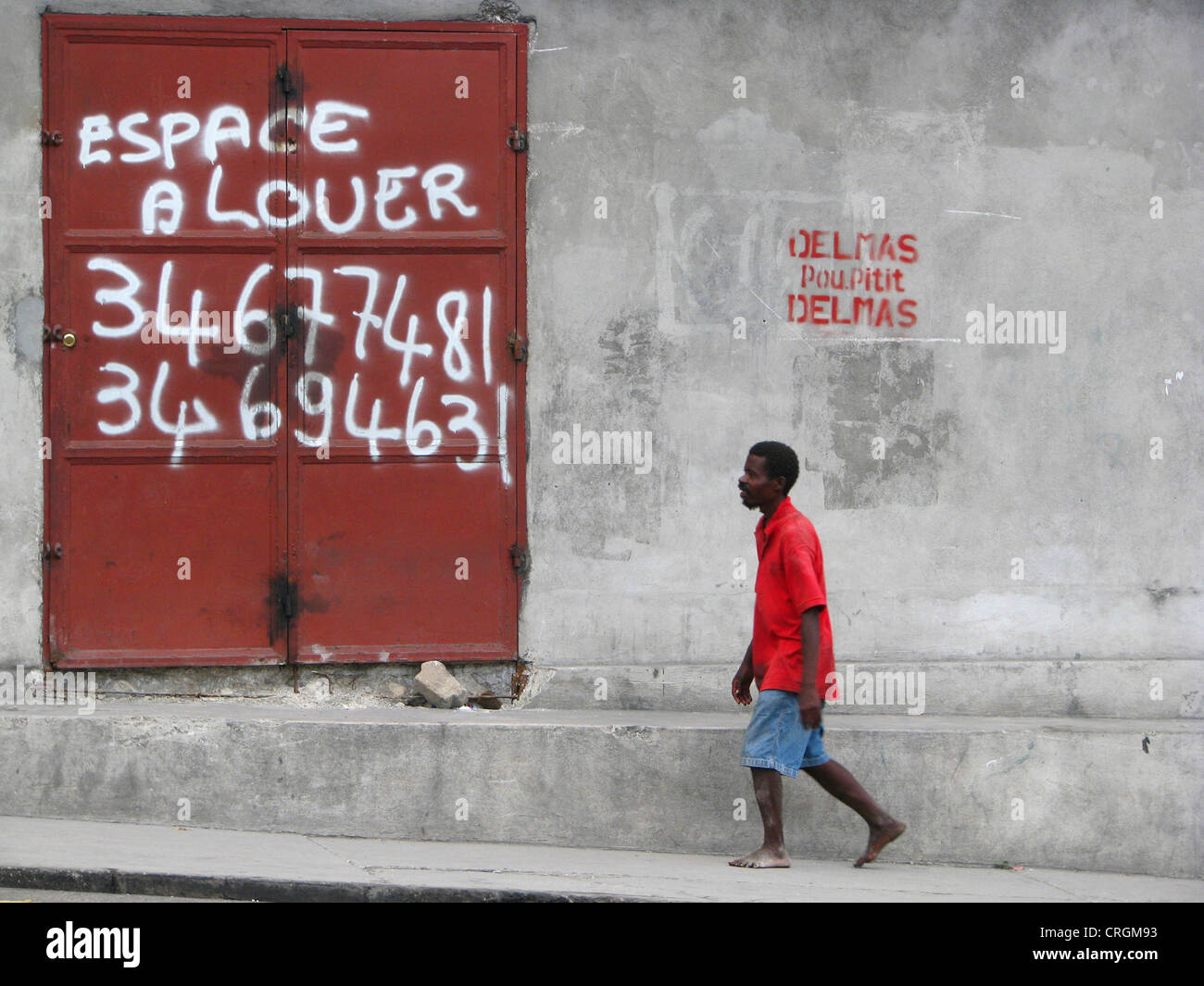 Mann zu Fuß entlang einer Betonwand mit einer eisernen Tür bietet Platz für Miete, Haiti, Provinz de l ' Ouest, Delmas, Port-Au-Prince Stockfoto
