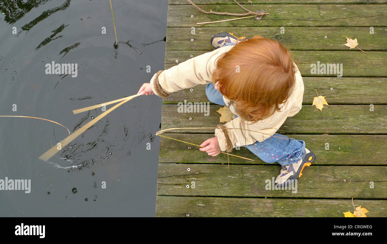 Kind sitzt auf einem Holzsteg Reed ins Wasser eintauchen Stockfoto