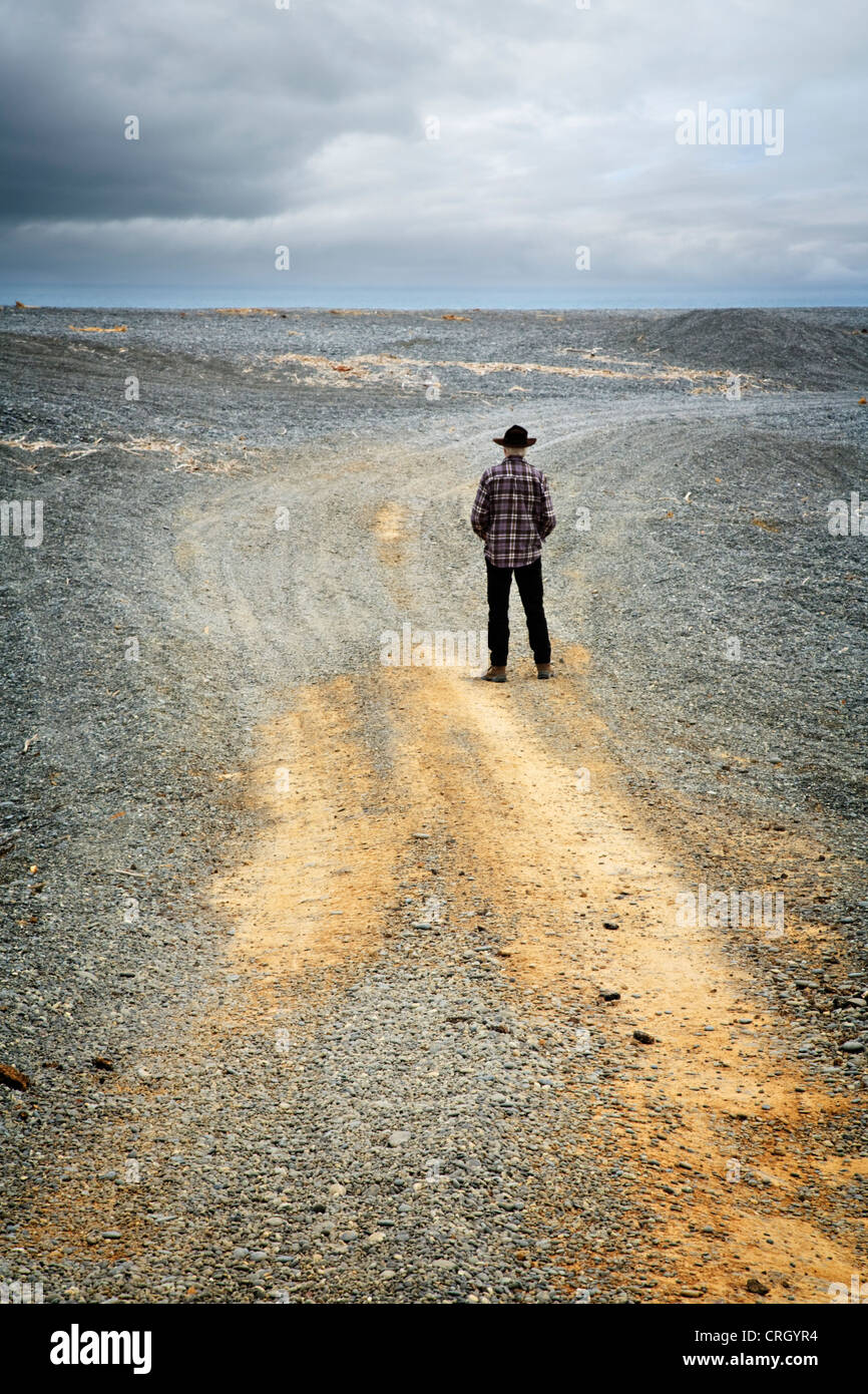 Lässig, älterer Mann, Rückansicht, mit Hut, stehend in einer trostlosen Landschaft unter ein stimmungsvoller Himmel. Model-Release verfügbar Stockfoto