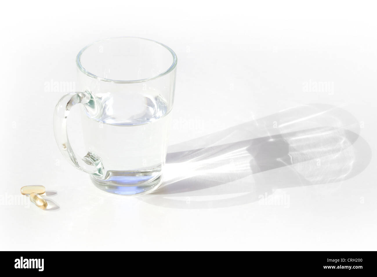 Tasse Wasser mit Pillen auf weißen Tisch mit Schatten Stockfoto