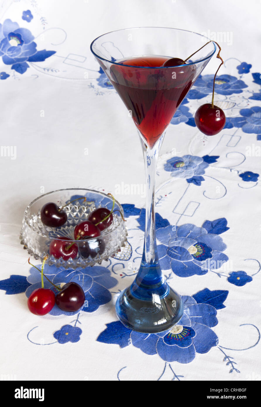 Baccarat Glas, lange ergab sich mit Fruchtsaft und Kirschen auf blau Applikation bestickte Tischdecke. Stockfoto