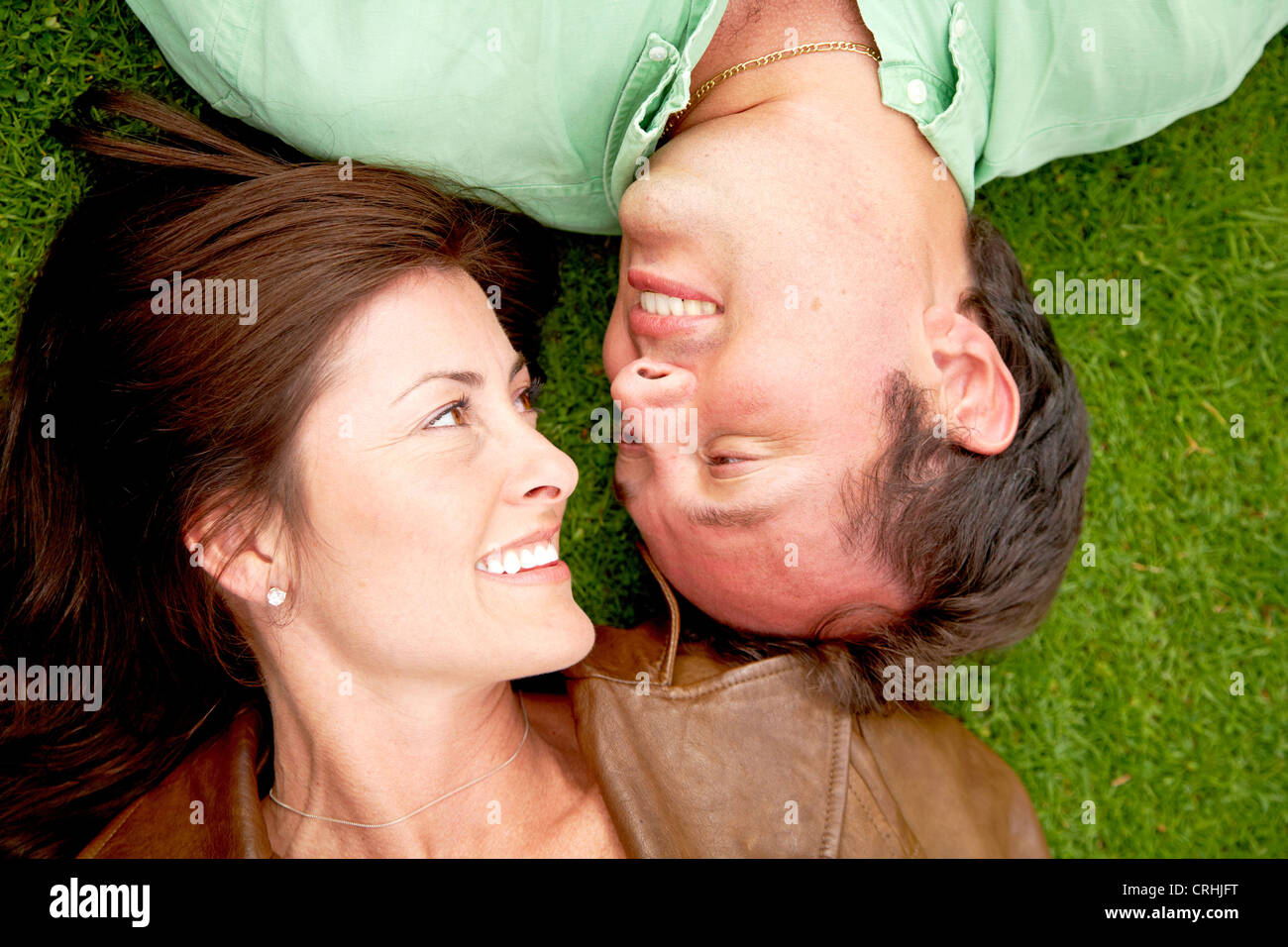 glückliches Paar liegen Kopf an Kopf auf dem Rasen, Lächeln, sahen einander Stockfoto