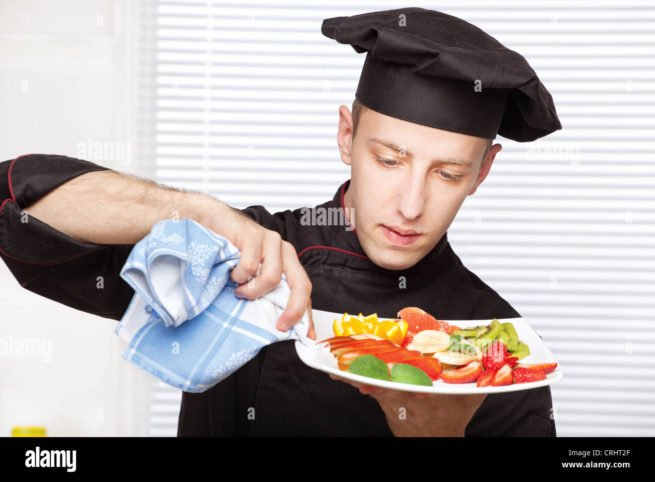 Koch in schwarzer Uniform Rand des einen Obstteller mit Tuch reinigen Stockfoto