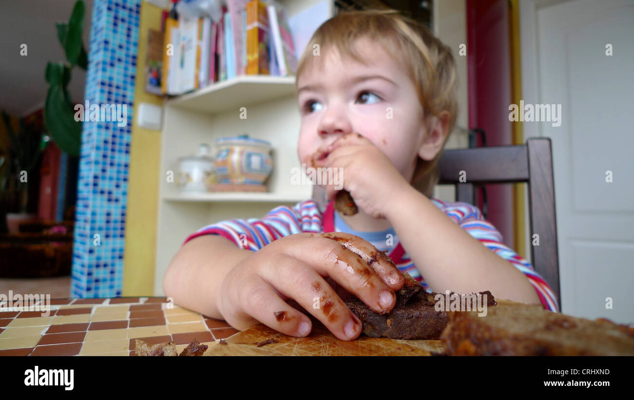 kleiner Junge mit Haselnuss-Creme-Brot und fettigen Gesicht und Hände Stockfoto