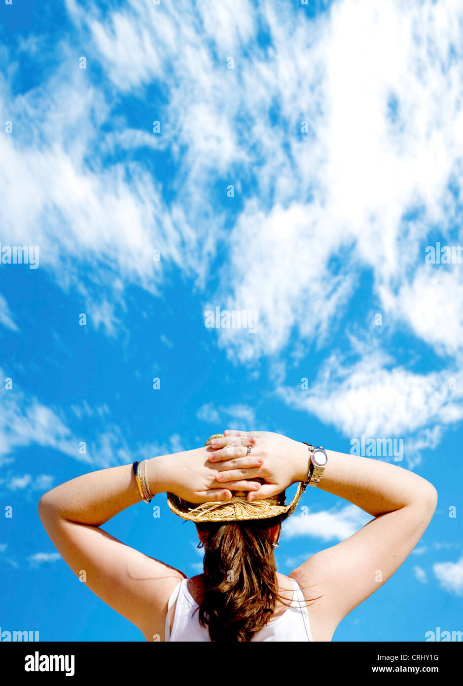 Frau mit langen Haaren und Sonnenhut, entspannen im Freien vor einem schönen blauen Himmel, die Hände auf den Kopf Stockfoto