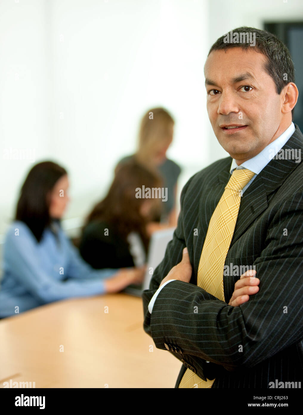 Business-Mann mit verschränkten Armen und Menschen im Hintergrund arbeitet an einem laptop Stockfoto