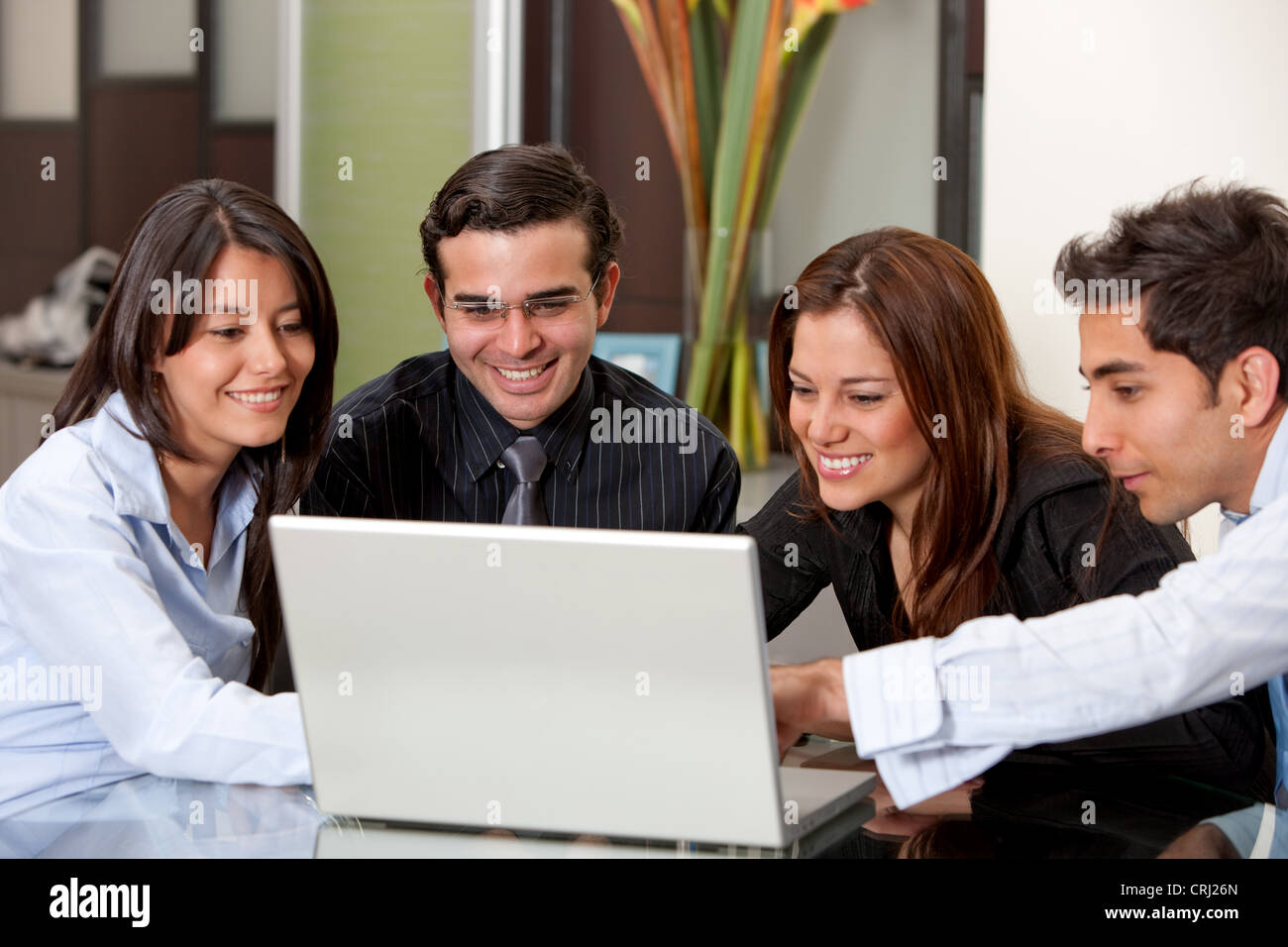 4 lächelnde junge Geschäftsleute um einen laptop Stockfoto