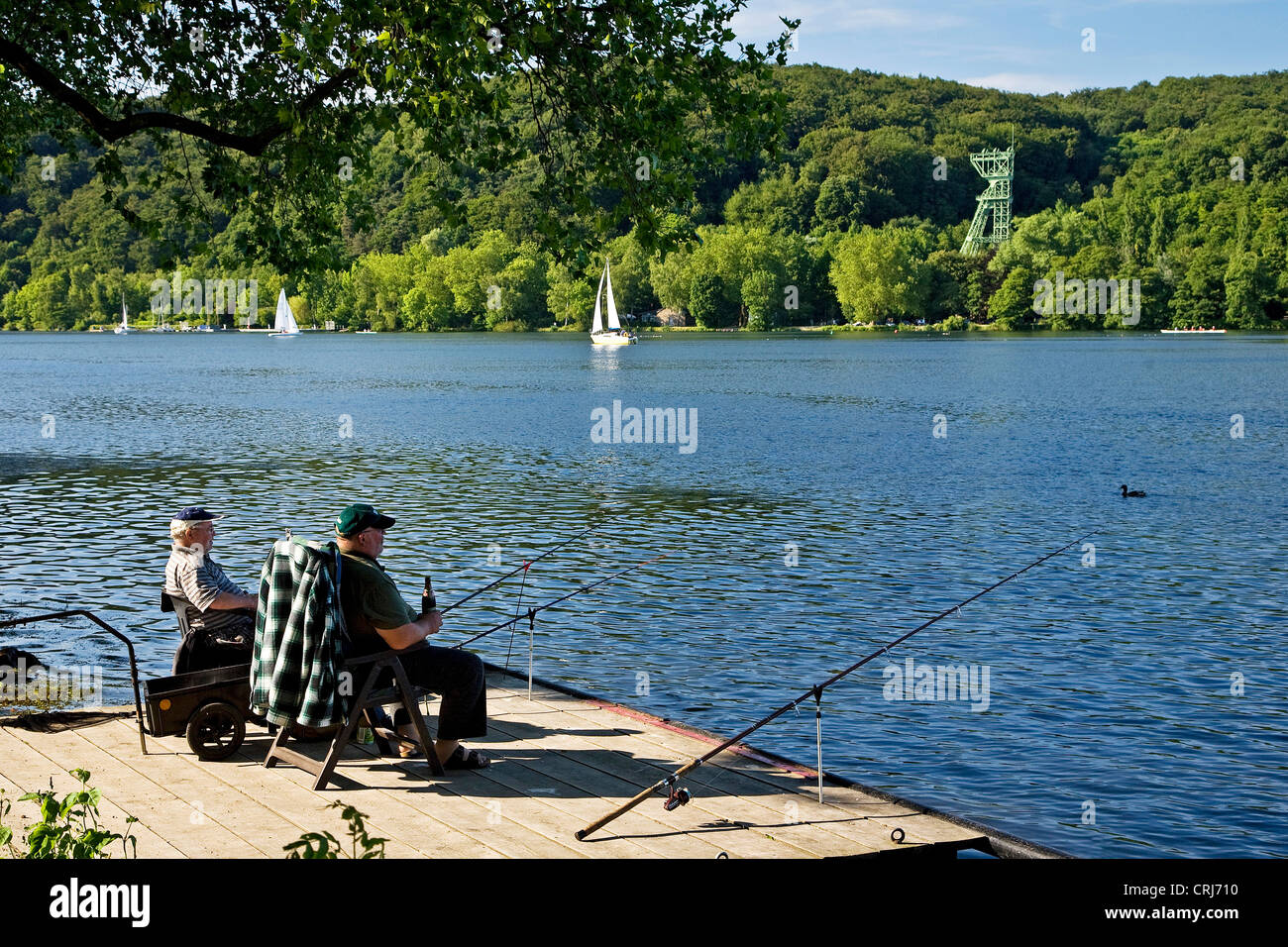 zwei Angler sitzen auf einem Holzsteg am See Baldeney, alte Kohle abbauen Carl Funke im Hintergrund, Essen, Ruhrgebiet, Nordrhein-Westfalen, Deutschland Stockfoto