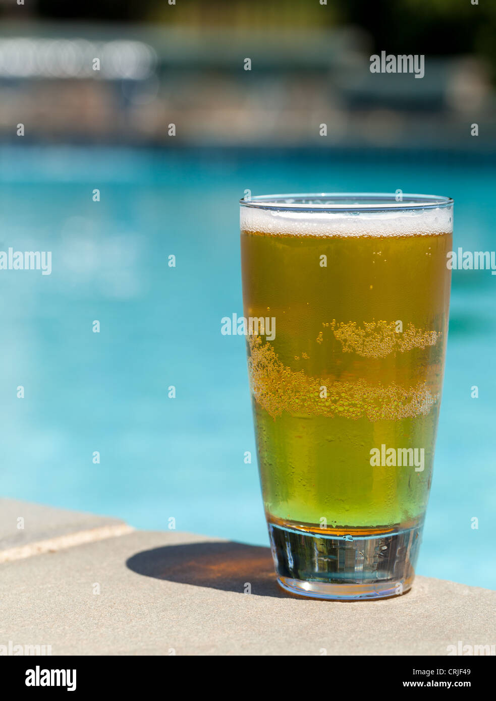 Schlichte Pint Glas kaltes Lager Bier sitzen am Rand des blauen Swimmingpool Stockfoto