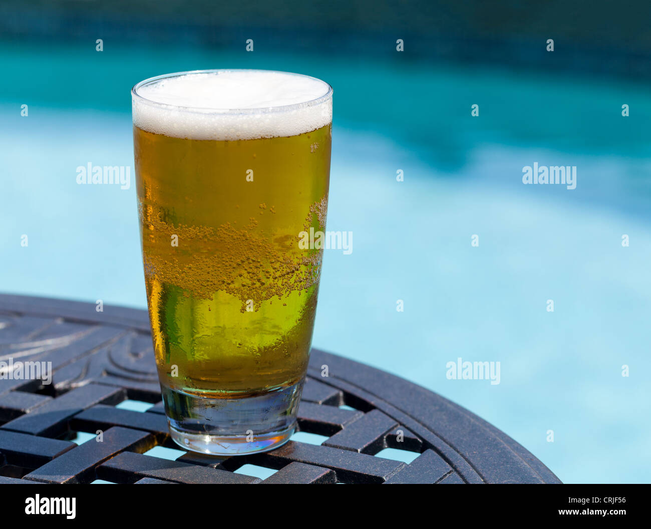 Schlichte Pint Glas kalten Lagerbier auf Tisch von blauen Swimmingpool Stockfoto