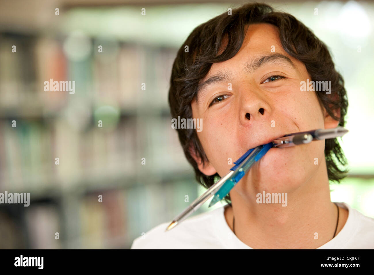 Student in einer Bibliothek mit seinem Mund voll von Kugelschreiber und Bleistifte Stockfoto