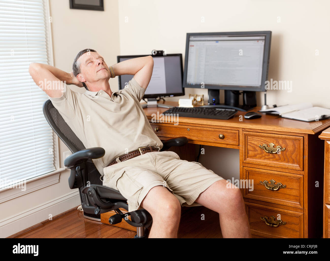 Menschen arbeiten von zu Hause Büro / Denken / Hinterherhängt/schlafen/Ausruhen in Shorts mit Schreibtisch mit zwei Monitoren Stockfoto