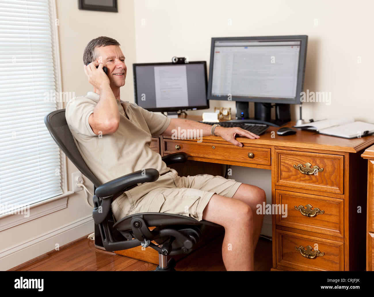 Menschen arbeiten von zu Hause Büro in Shorts mit Schreibtisch mit zwei Monitoren auf dem Telefon Stockfoto