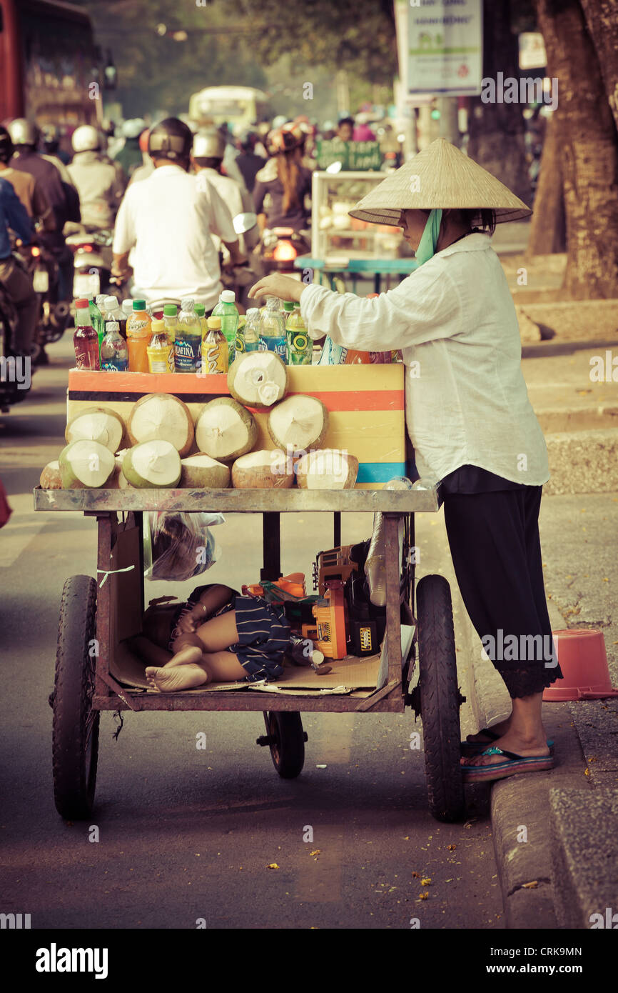 Kokos-Verkäufer auf einer Straße in HCMC, Vietnam. Die lustige Seite hier ist ihr Kind ein Nickerchen in einem speziellen Fach angeordnet Stockfoto