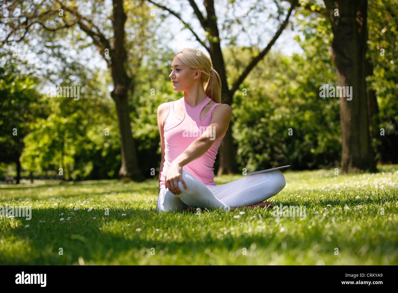 Eine junge, blonde Frau auf der Wiese sitzen, stretching Stockfoto