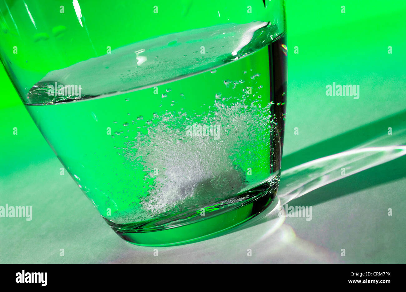 Tablette löst sich in ein Glas Wasser vor einem grünen Hintergrund. Stockfoto