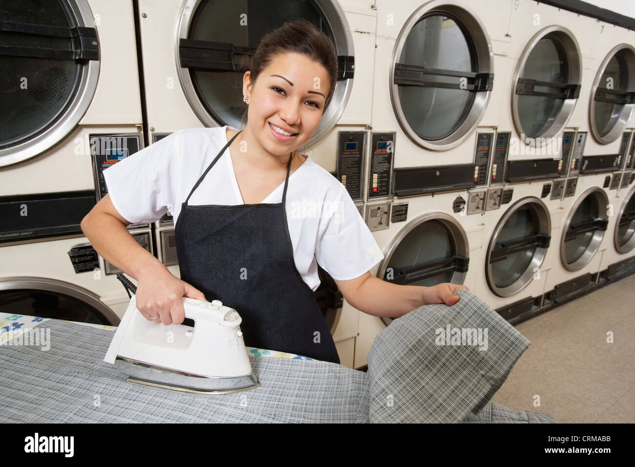 Porträt einer glücklichen Frau mit Schürze Bügeln vor Waschmaschinen Stockfoto