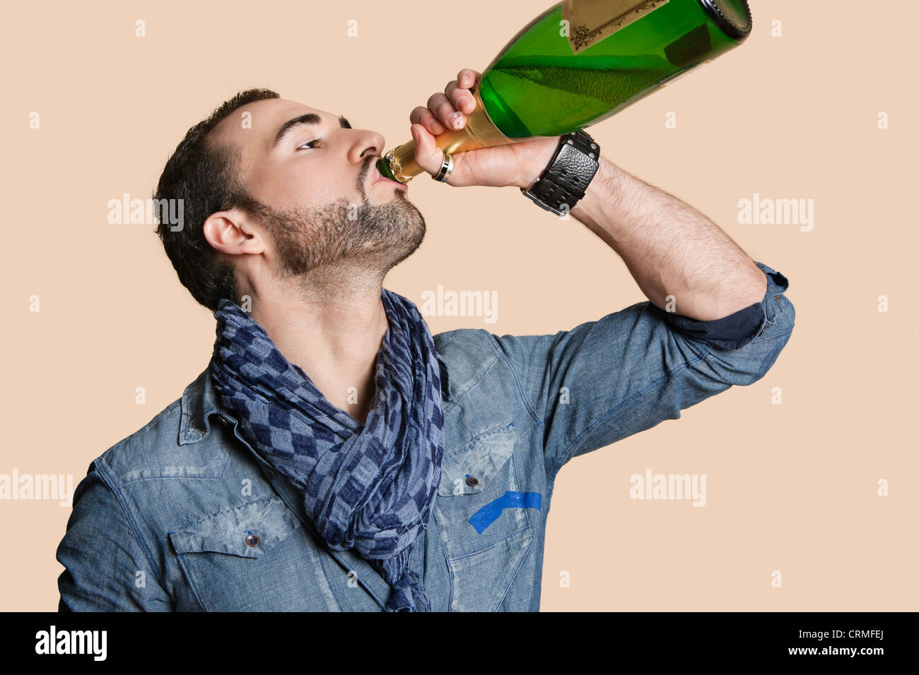 Junger Mann trinken Champagner aus der Flasche über farbigen Hintergrund Stockfoto