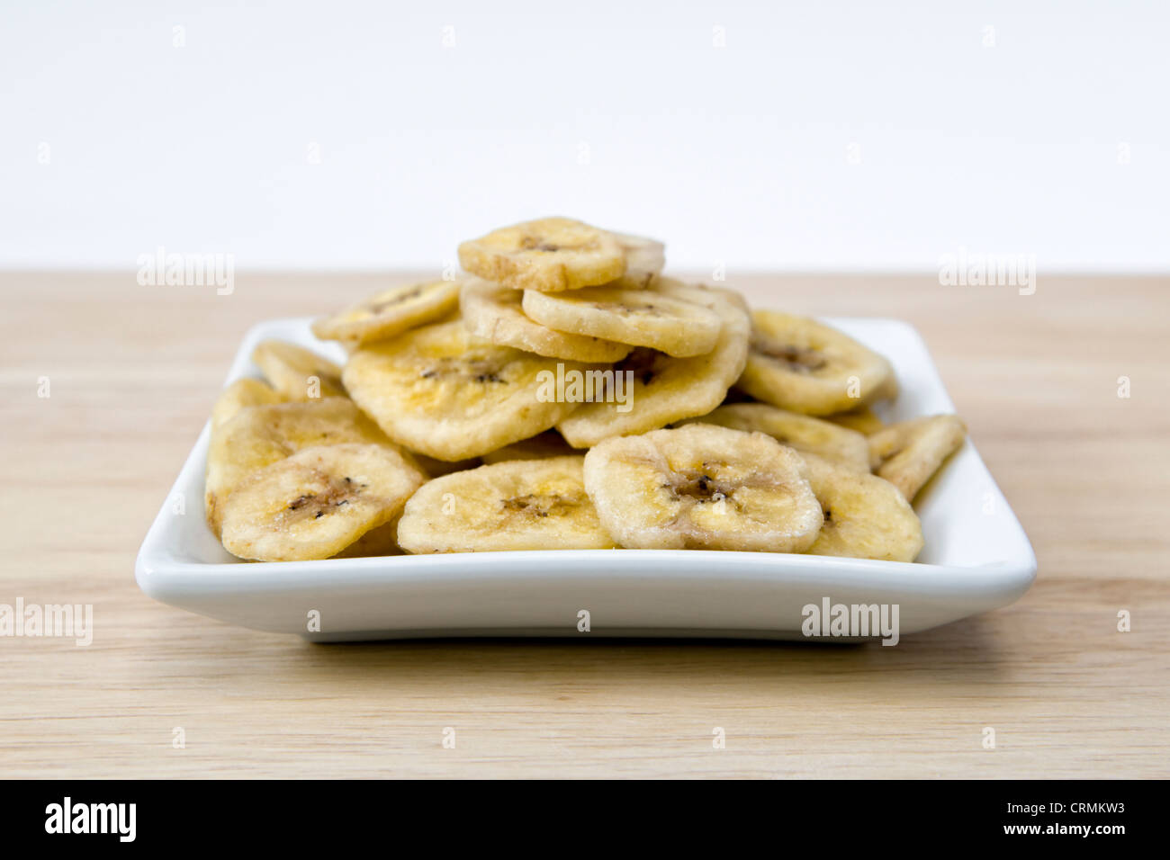 Getrocknete Bananenchips auf Schneidbrett aus Holz auf einem weißen Hintergrund Stockfoto