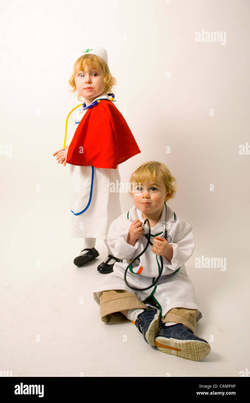 Ein Mädchen gekleidet als Krankenschwester hinter ein kleiner Junge, als Arzt verkleidet, wie er auf dem Boden sitzt. Stockfoto