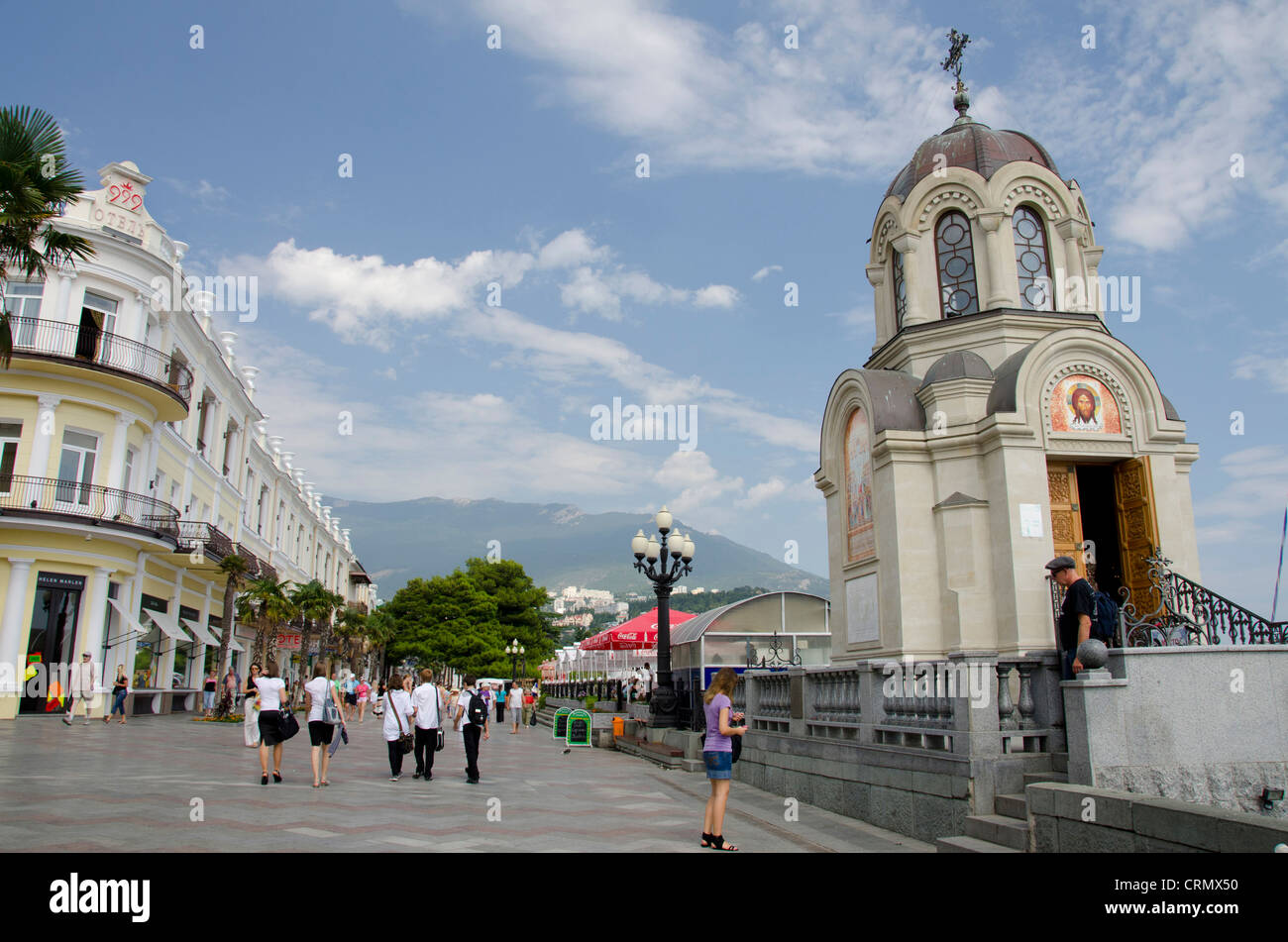 Ukraine, Yalta. Waterfront Fussgängerzone Gehweg entlang dem Schwarzen Meer mit kleinen Kapelle. Krim-Berge in der Ferne. Stockfoto