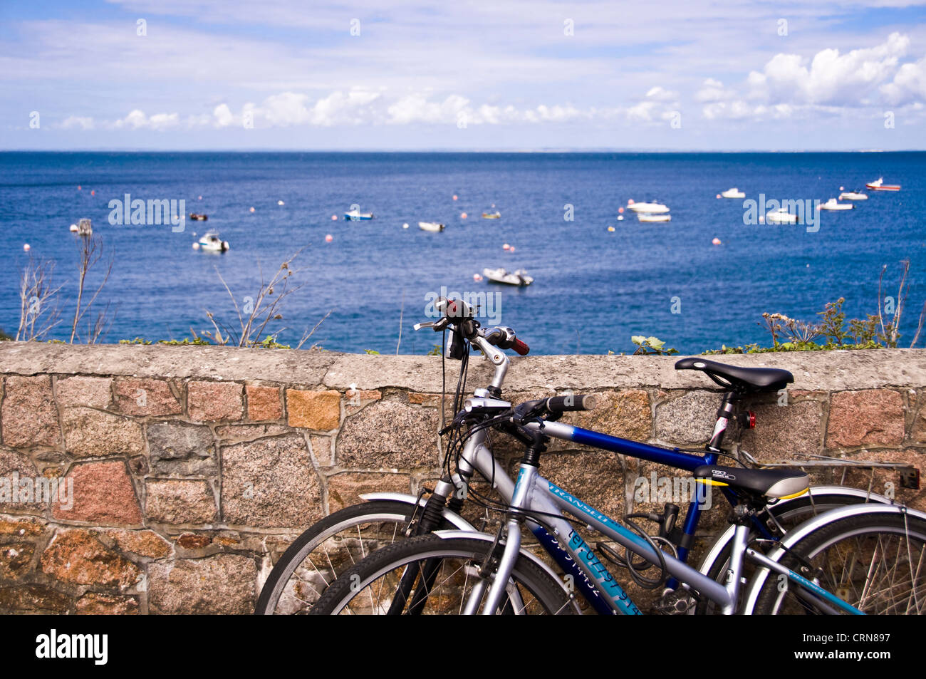 Zwei Fahrräder geparkt entlang einer Straße gegen eine Wand mit Blick aufs Meer - Jersey-Insel Stockfoto