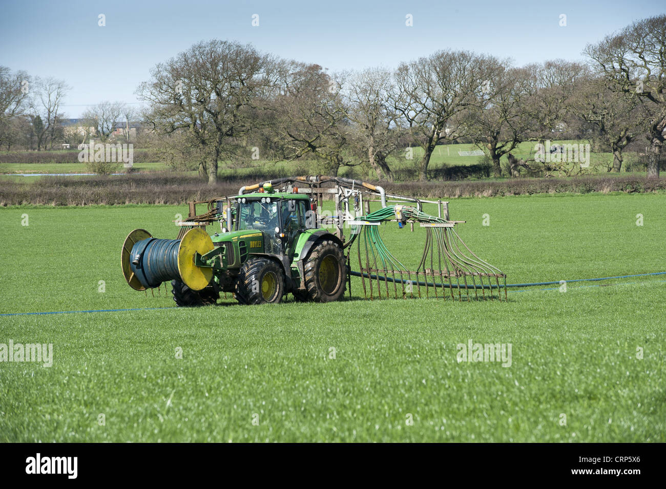 John Deere Traktor mit Nabelschnur Gülle Streuer, Verbreitung von Gülle in Weiden, Winmarleigh, Lancashire, England, März Stockfoto