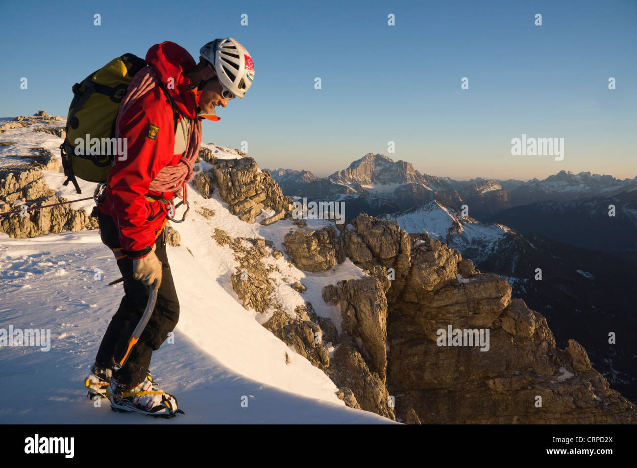 Männliche Bergsteiger in rote Jacke erreicht verschneiten Gipfel des Lagazuoi, nach unten ins Tal Stockfoto