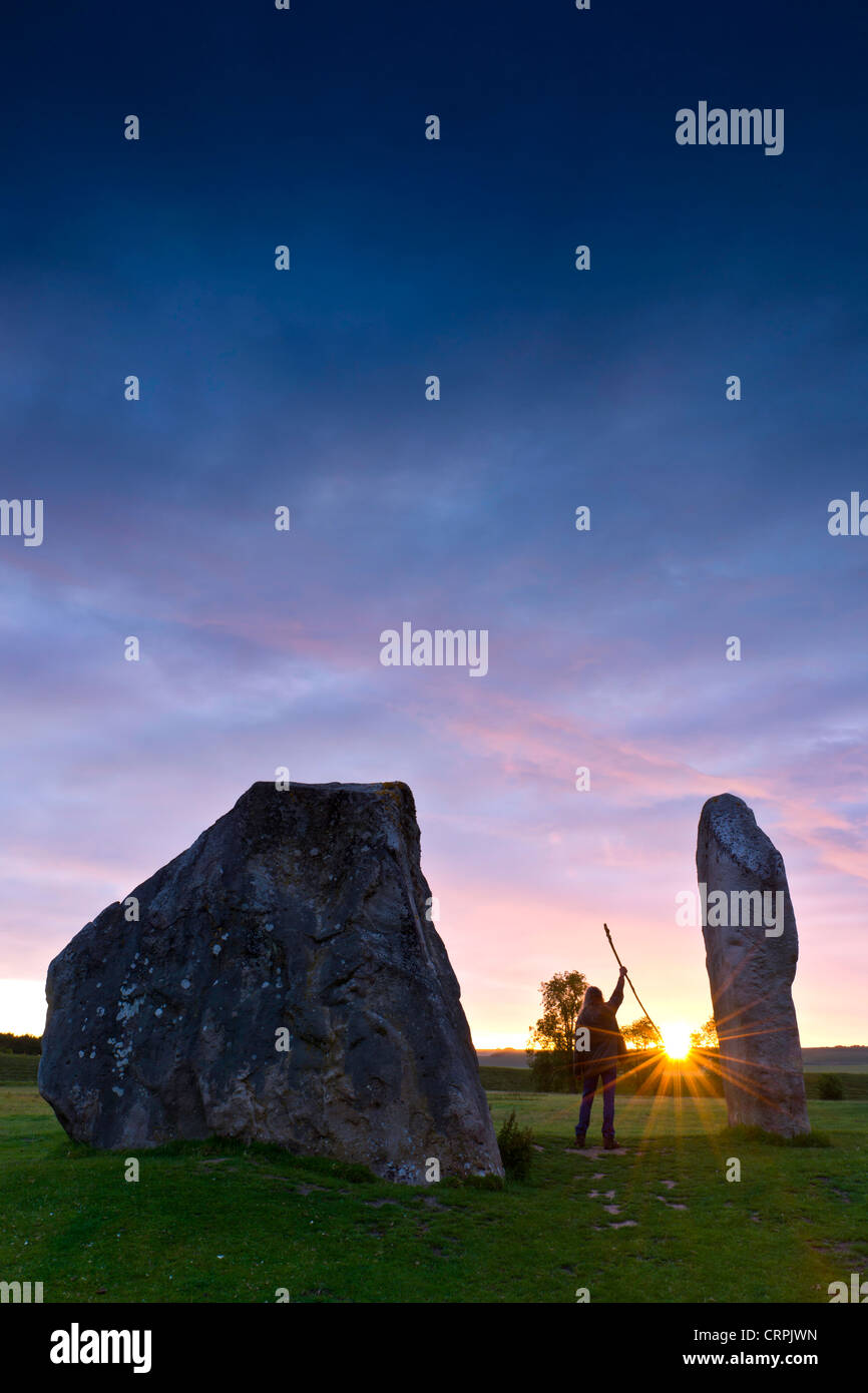 Person, die einen Mitarbeiterstamm Gruß den Sonnenaufgang während der Sommersonnenwende in den Avebury ring, der älteste Stein bekannt Stockfoto