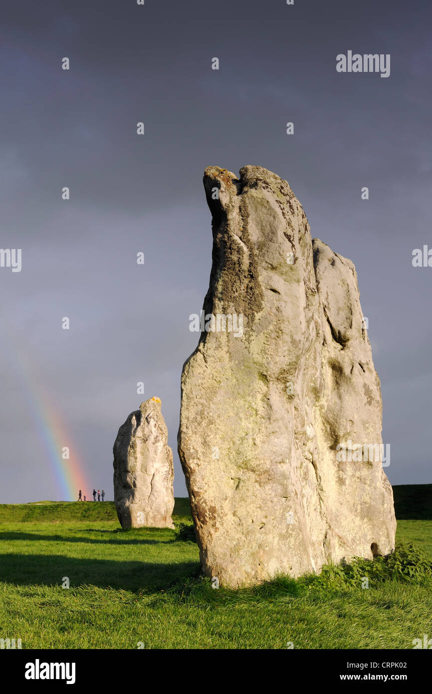 Stehenden Steinen, Teil von Avebury Ring, mit dem Ende eines Regenbogens fällt auf eine Gruppe von Menschen im Hintergrund. Stockfoto