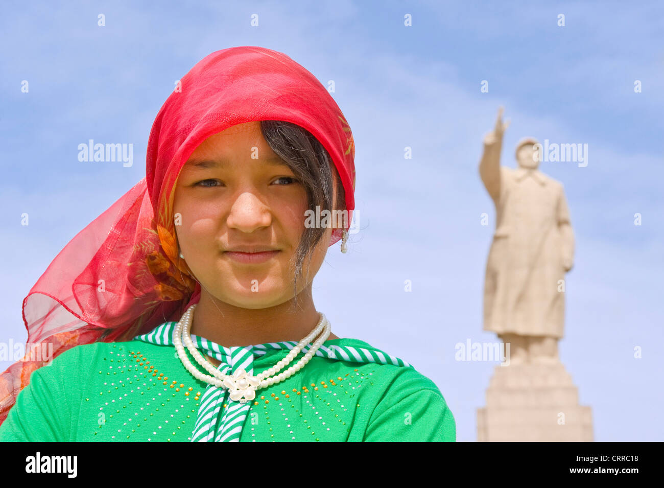 Eine junge Chinesin Uyghur posieren für die Kamera mit der Statue von Mao Zedong hinter in Kashgar. Stockfoto