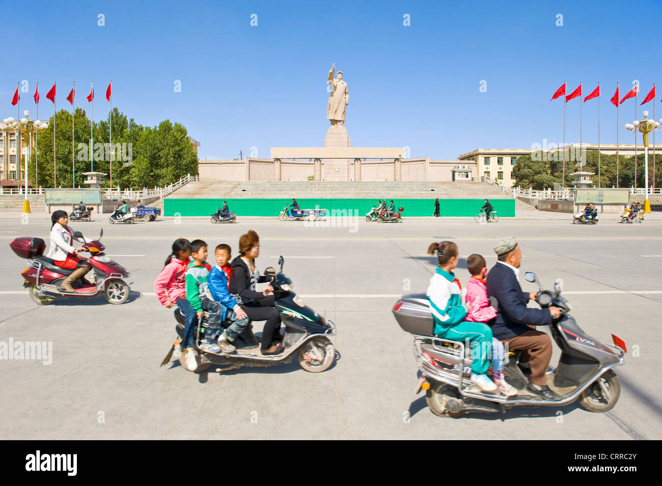 Mit Bewegungsunschärfe.  Fahrzeuge und Personen reisen Sie vorbei an der Statue von Mao Zedong gegenüber dem Stadtplatz in Kashgar. Stockfoto