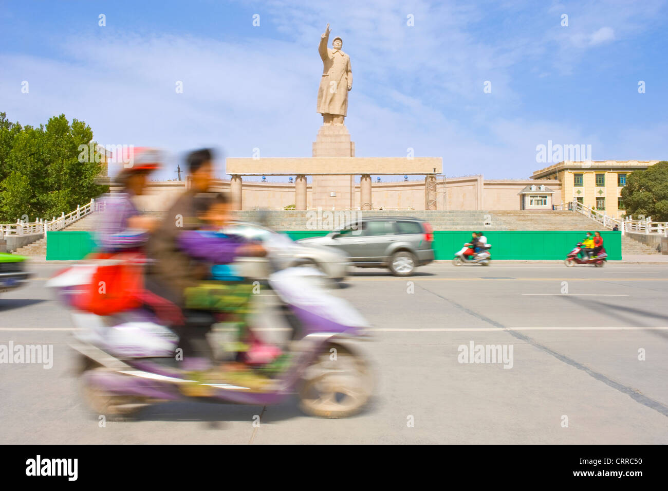 Mit Bewegungsunschärfe.  Fahrzeuge und Personen reisen Sie vorbei an der Statue von Mao Zedong gegenüber dem Stadtplatz in Kashgar. Stockfoto