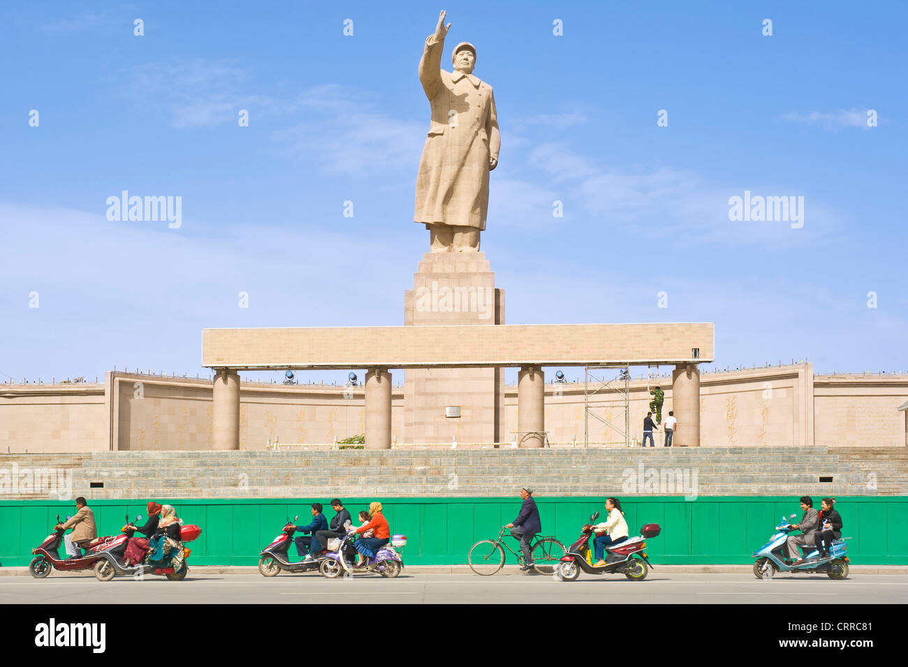 Mit Bewegungsunschärfe.  Fahrzeuge und Personen reisen Sie vorbei an der Statue von Mao Zedong gegenüber dem Stadtplatz in Kashgar. Stockfoto