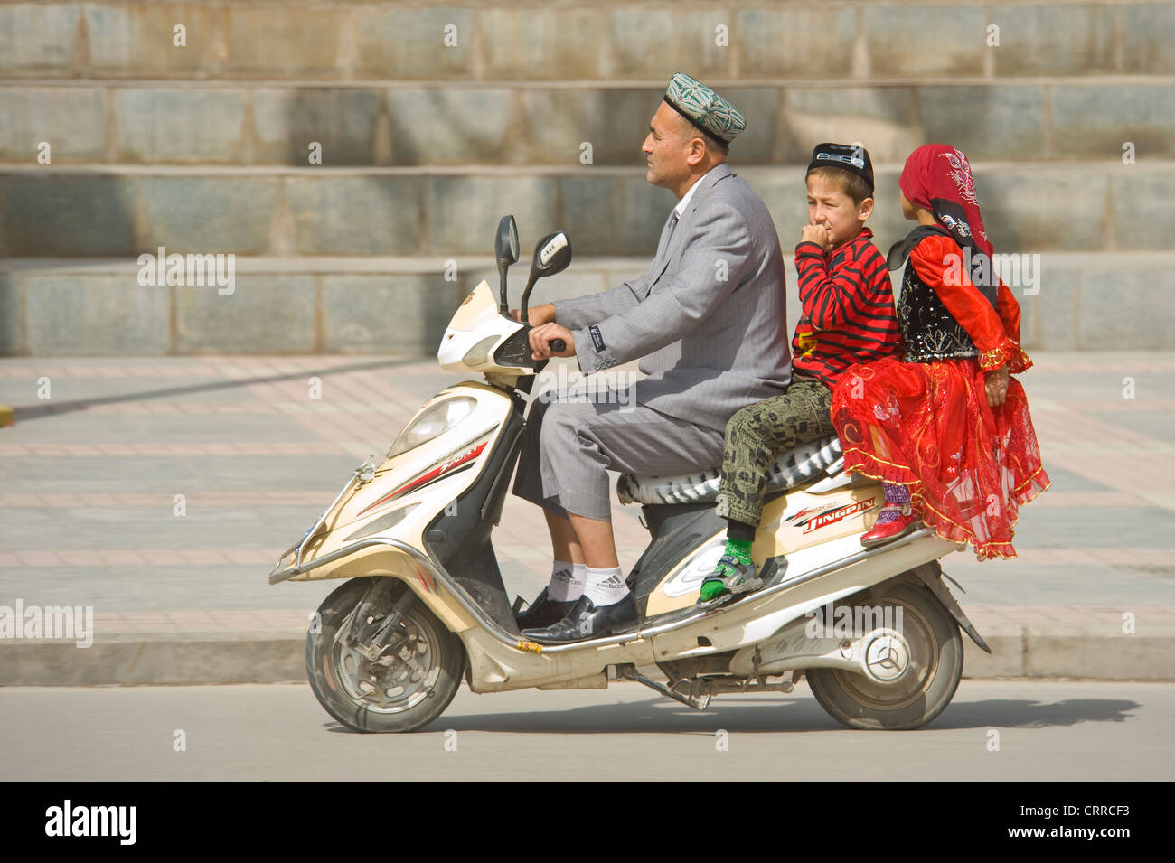 Eine chinesische Uygher Vater und 2 Kinder reist entlang einer Straße auf ihren Roller in Kashgar. Stockfoto