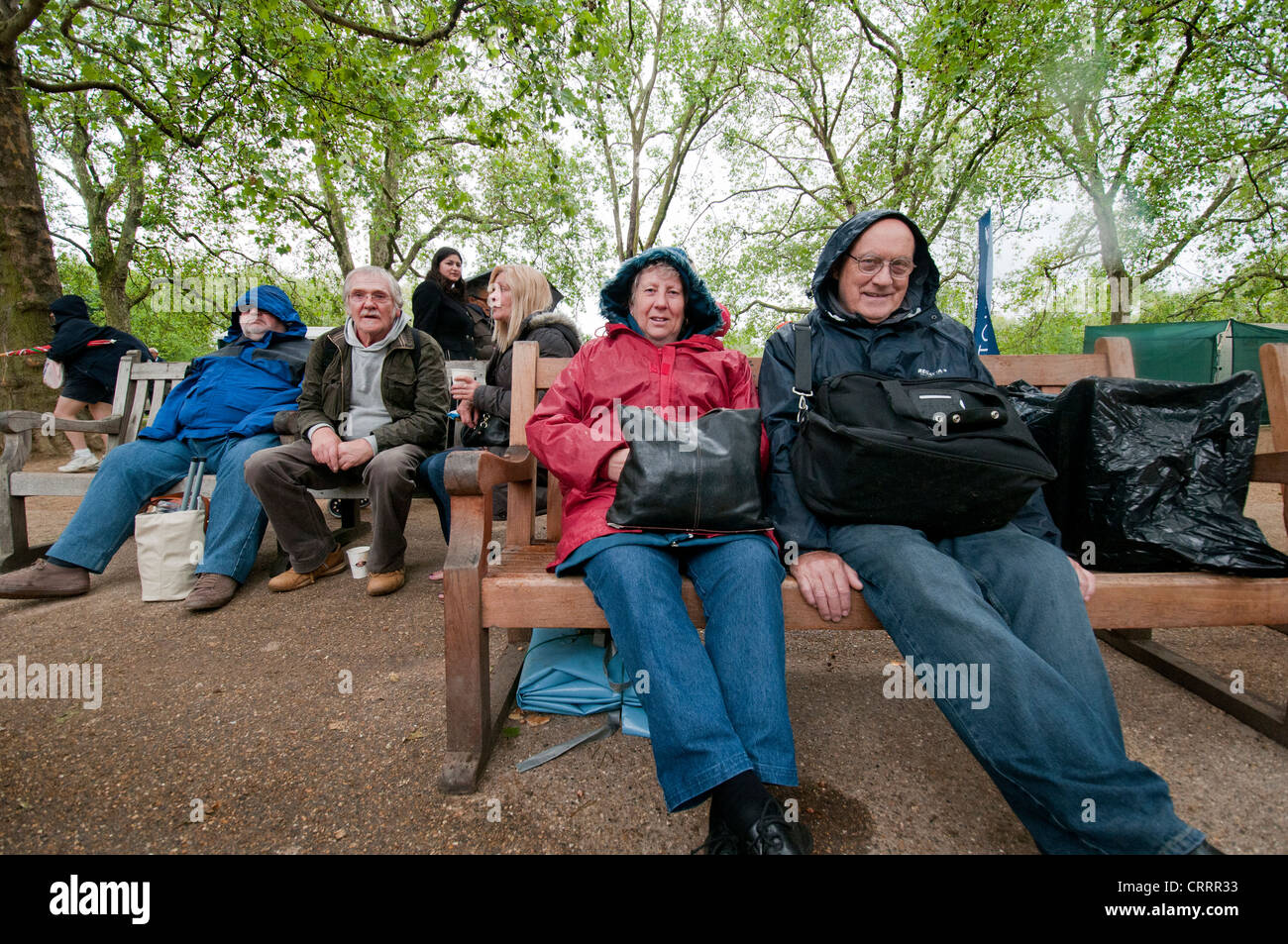 Menschen mittleren Alters sitzen auf den Bänken im Park Regenwetter Stockfoto