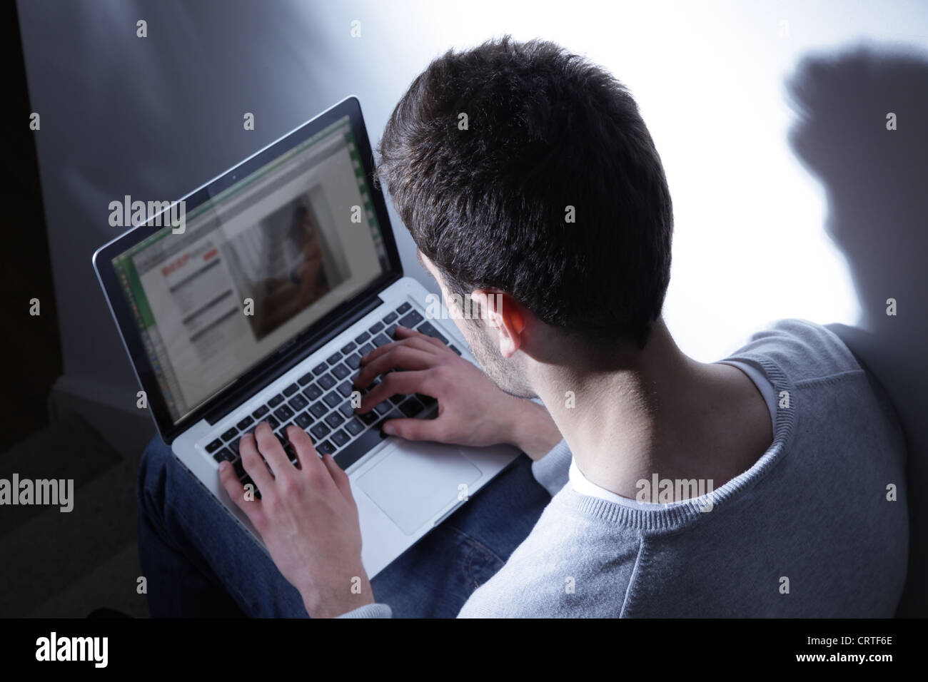 Junger Mann sitzt in der Dunkelheit mit seinem Laptop auf eine generische Website. Stockfoto