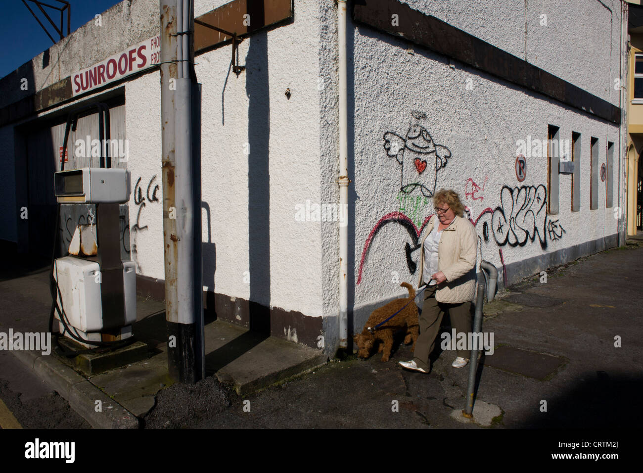 Eine Frau geht ihren Hund vorbei eine geschlossene Garage Räumlichkeiten in der Stadt Galway, Irland. Stockfoto