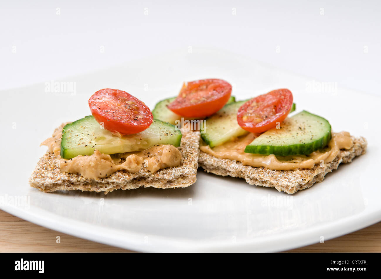 Knusprige Brot mit Erdnussbutter, in Scheiben geschnittenen Gurken und Tomaten auf weißen Teller mit Gewürzen obenauf Stockfoto