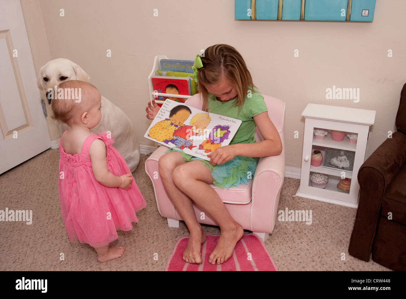 Zehn Jahre altes Mädchen liest ein Buch auf ihre Babyschwester zu Hause. Stockfoto