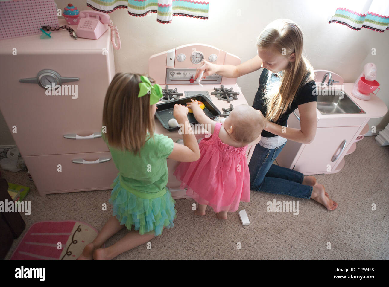 Zwei ältere Schwestern mit einjähriger Geschwister im Rollenspiel Küche zu Hause zu spielen. Stockfoto