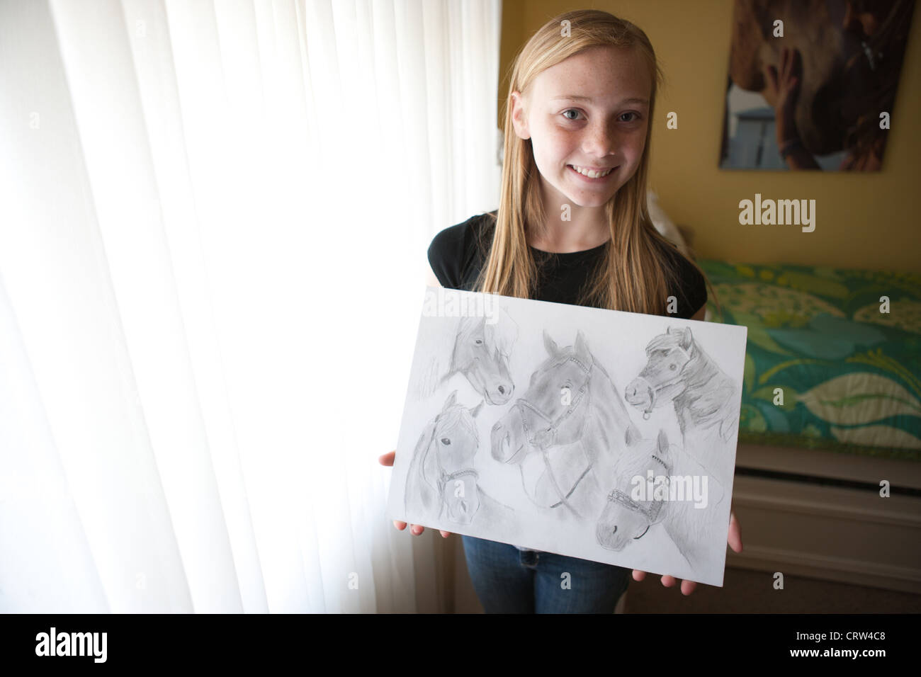 13 Jahre altes Mädchen hält ihre Bleistiftzeichnungen von Pferden und lächelt in die Kamera. Stockfoto