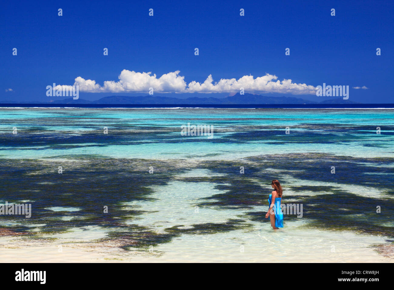 Frau in blau Sarong watet in den Gewässern in der Nähe von Anse Source d ' Argent auf La Digue auf den Seychellen Stockfoto
