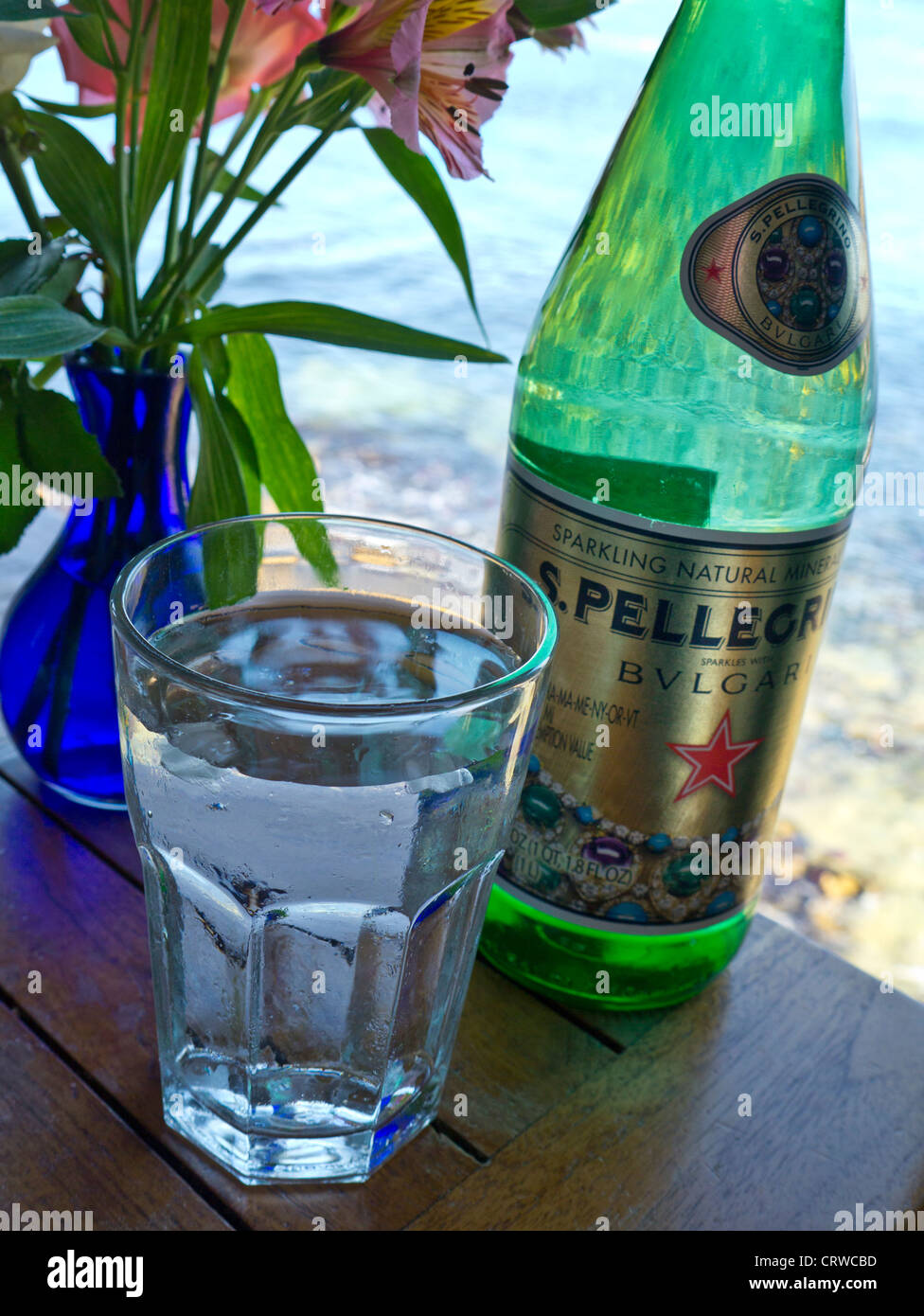 Pellegrino Bulgari Luxus in Flaschen Wasser und Glas auf floral Restauranttisch mit Blick aufs Meer Stockfoto
