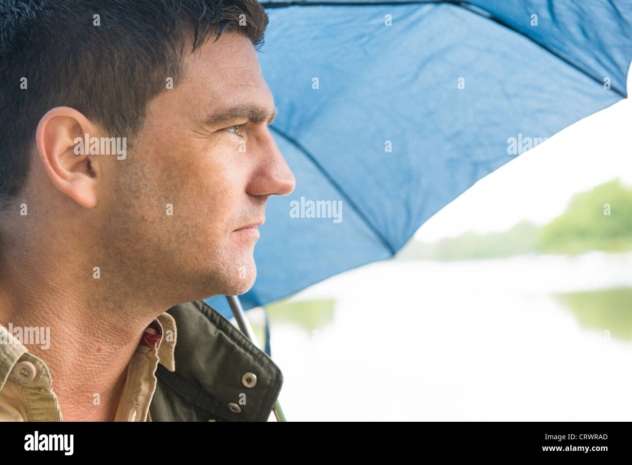 Mann mit einem blauen Schirm im Regen stehen und blickte über einen See Stockfoto