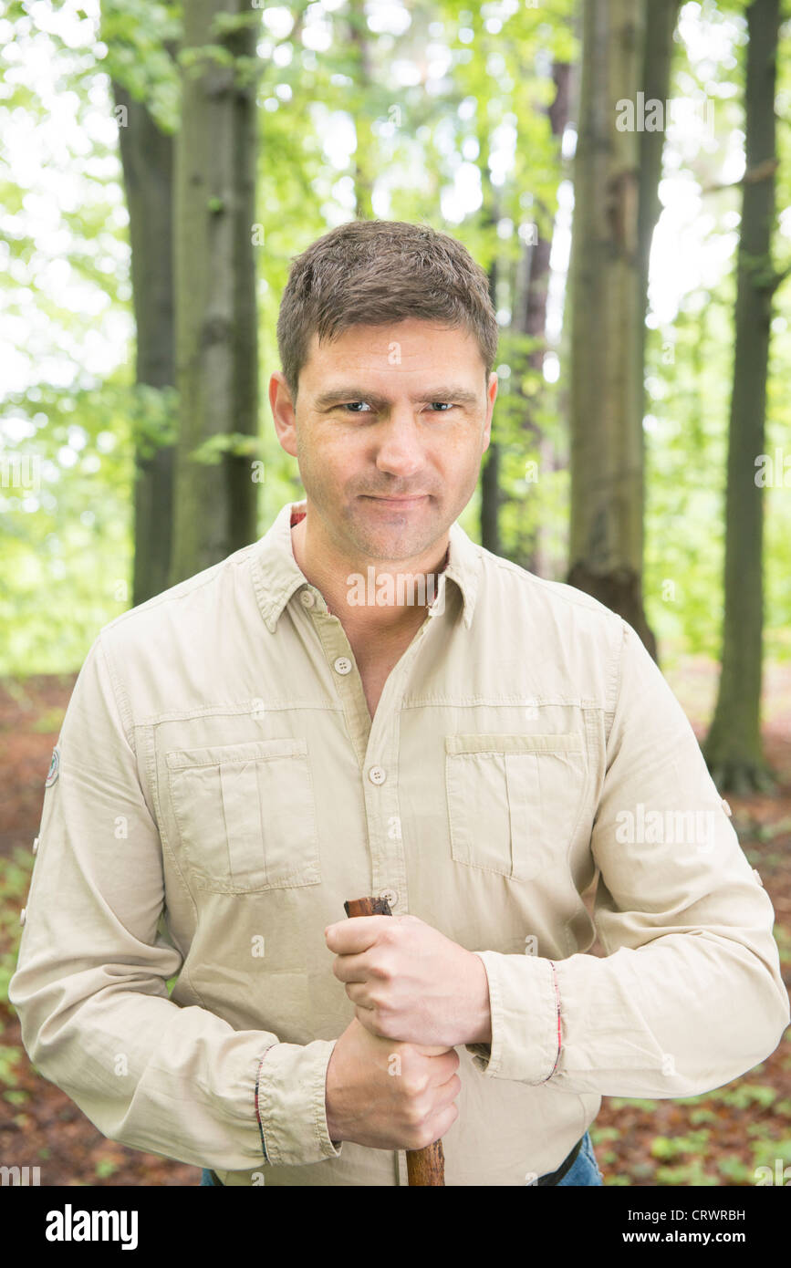 Mitte erwachsenen Mann, der in einem Wald hält einen Spazierstock und schaut in die Kamera Stockfoto