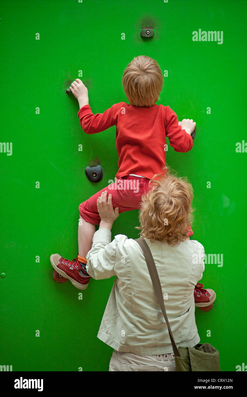 kleiner Junge Klettern eine Kletterwand, unterstützt von seiner Mutter Stockfoto