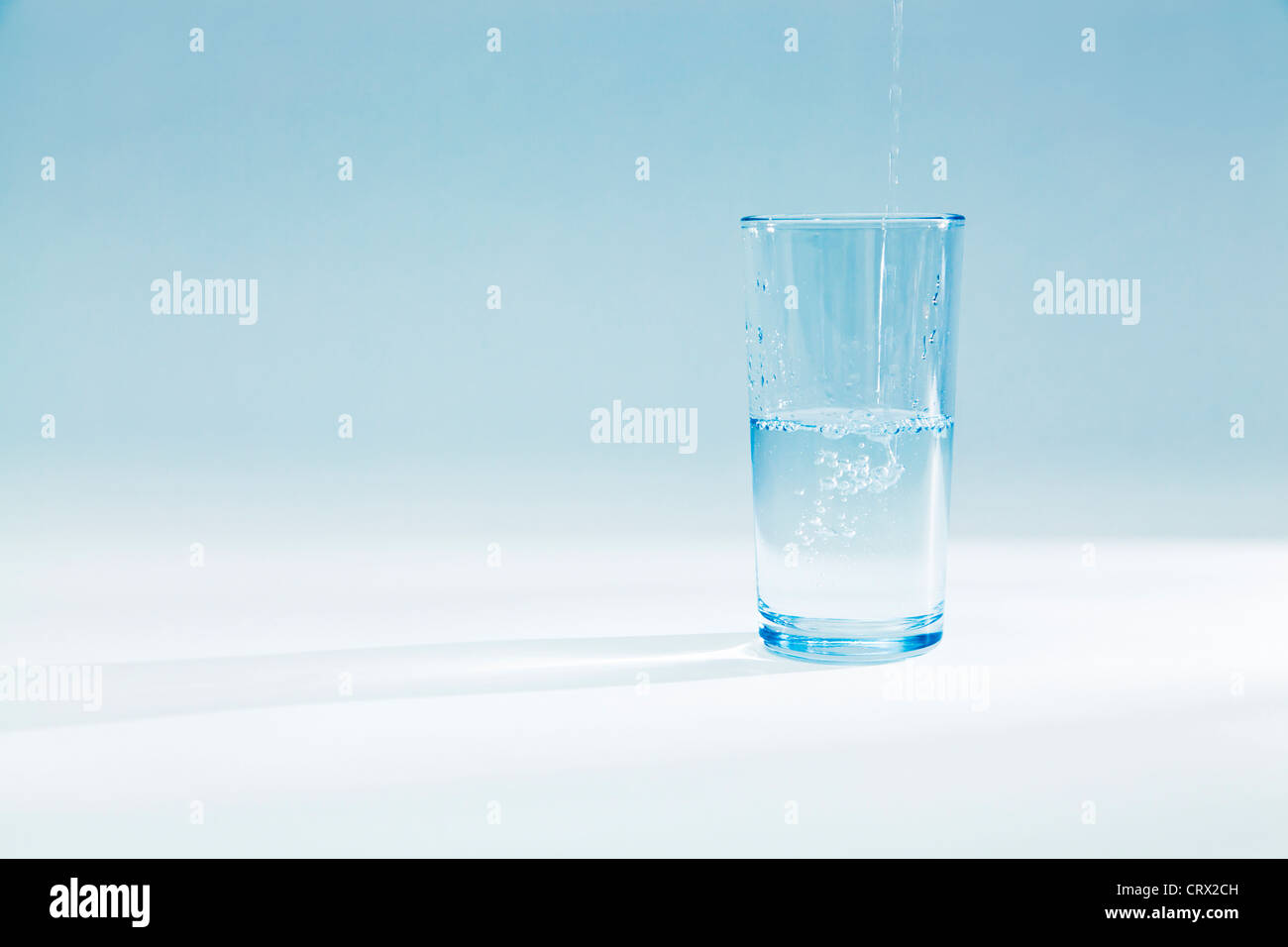 Wasser gießen in ein halb volles Glas Becher in ein blaues Licht Stockfoto